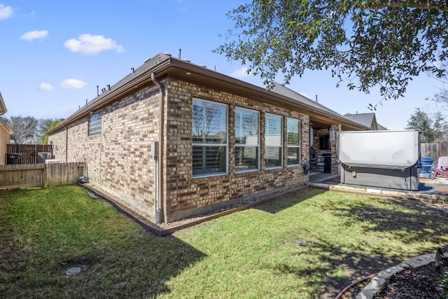 rear view of house featuring a yard, brick siding, fence, and a hot tub