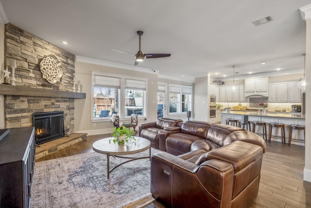 living area featuring visible vents, a ceiling fan, ornamental molding, light wood-type flooring, and a fireplace