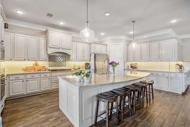 kitchen with decorative light fixtures, a center island with sink, and white cabinetry