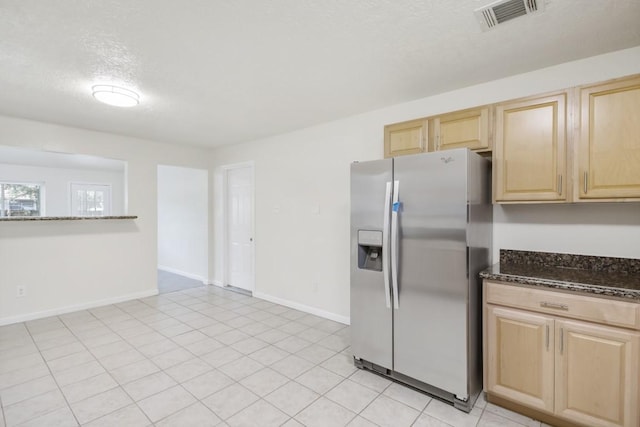 kitchen featuring visible vents, baseboards, stainless steel refrigerator with ice dispenser, dark stone counters, and light brown cabinetry