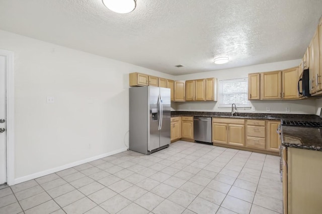 kitchen featuring baseboards, dark stone countertops, appliances with stainless steel finishes, and a sink