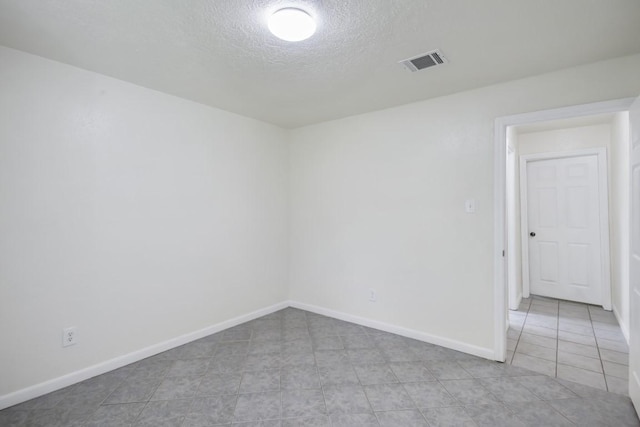 unfurnished room with a textured ceiling, light tile patterned floors, visible vents, and baseboards