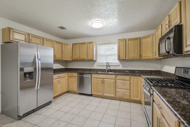 kitchen with light brown cabinets, a sink, visible vents, appliances with stainless steel finishes, and dark stone counters