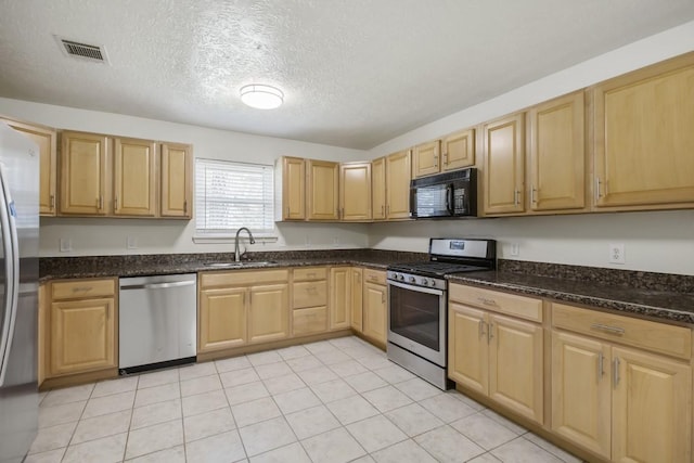 kitchen featuring a textured ceiling, stainless steel appliances, a sink, visible vents, and dark stone countertops