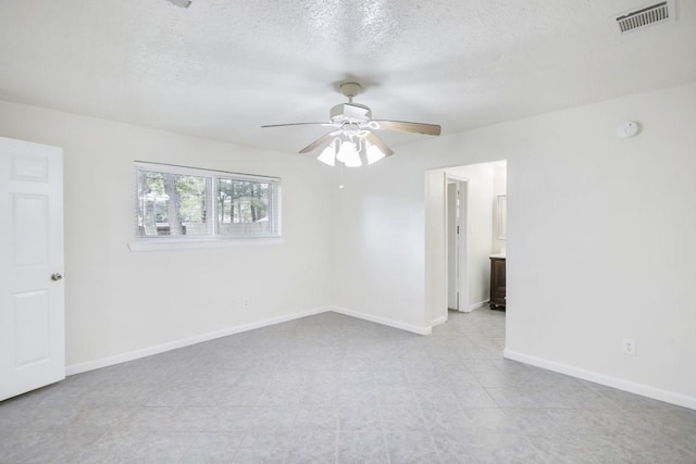 empty room with a ceiling fan, visible vents, a textured ceiling, and baseboards