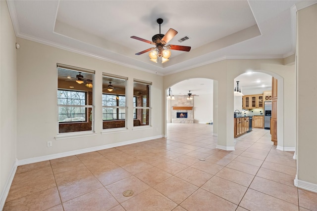 spare room featuring arched walkways, a raised ceiling, a brick fireplace, and light tile patterned floors