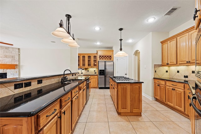 kitchen with visible vents, arched walkways, appliances with stainless steel finishes, glass insert cabinets, and a sink