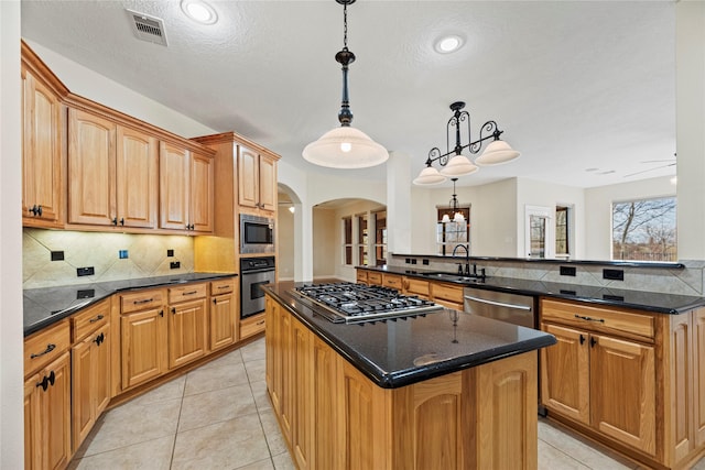 kitchen featuring arched walkways, a peninsula, stainless steel appliances, a sink, and decorative light fixtures