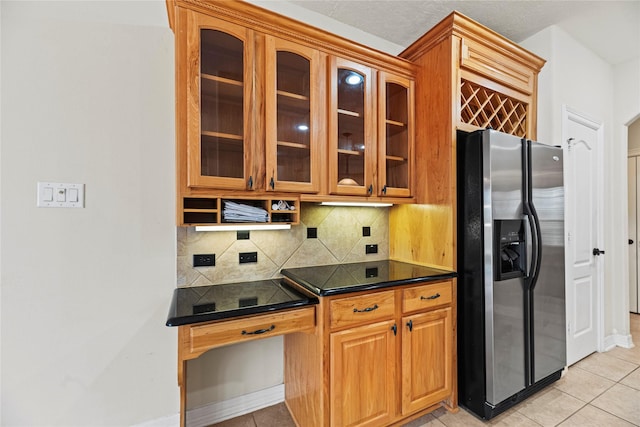 kitchen with backsplash, dark countertops, stainless steel fridge, and glass insert cabinets