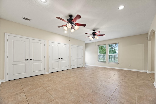 unfurnished bedroom with baseboards, visible vents, arched walkways, and multiple closets