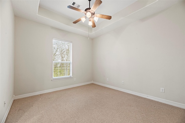 carpeted empty room featuring ceiling fan, baseboards, visible vents, and a raised ceiling