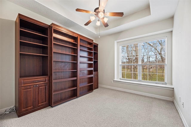 interior space with light carpet, a tray ceiling, a ceiling fan, and baseboards