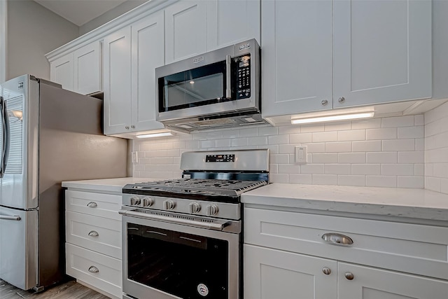 kitchen with tasteful backsplash, appliances with stainless steel finishes, white cabinetry, light stone countertops, and light wood-type flooring