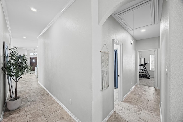 hallway featuring crown molding, stone tile floors, a textured wall, attic access, and baseboards