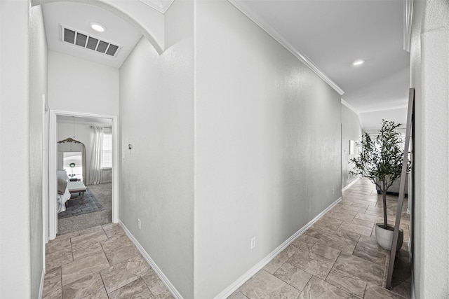 hall with arched walkways, crown molding, visible vents, stone finish flooring, and baseboards