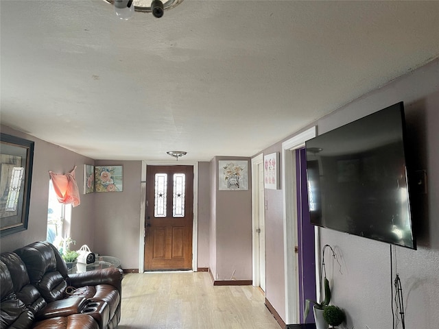 foyer entrance with light wood-style floors, a textured ceiling, and baseboards