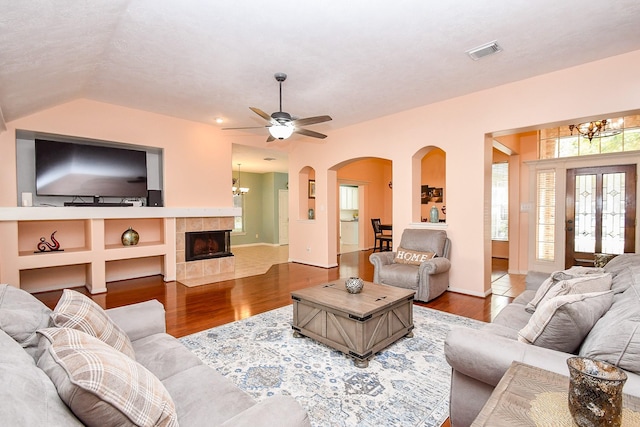 living area featuring a tile fireplace, visible vents, wood finished floors, and ceiling fan with notable chandelier