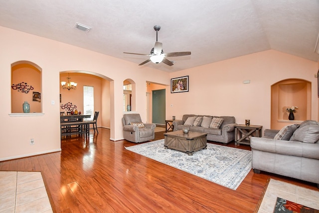 living area featuring ceiling fan with notable chandelier, visible vents, vaulted ceiling, and wood finished floors