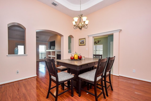 dining room featuring a tray ceiling, visible vents, an inviting chandelier, wood finished floors, and baseboards