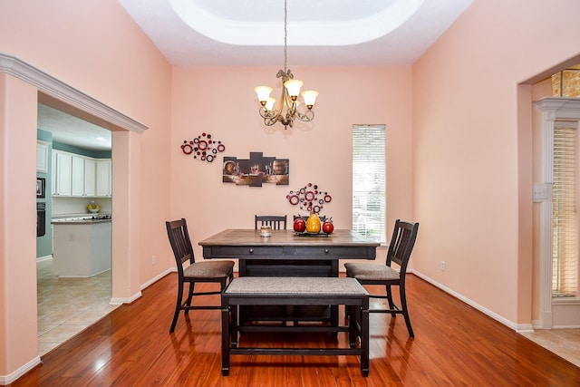 dining area with a raised ceiling, a notable chandelier, baseboards, and wood finished floors