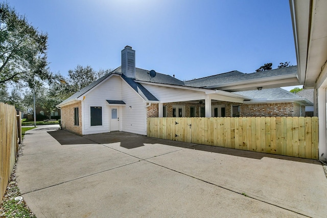 rear view of house featuring brick siding, a chimney, fence private yard, and a gate