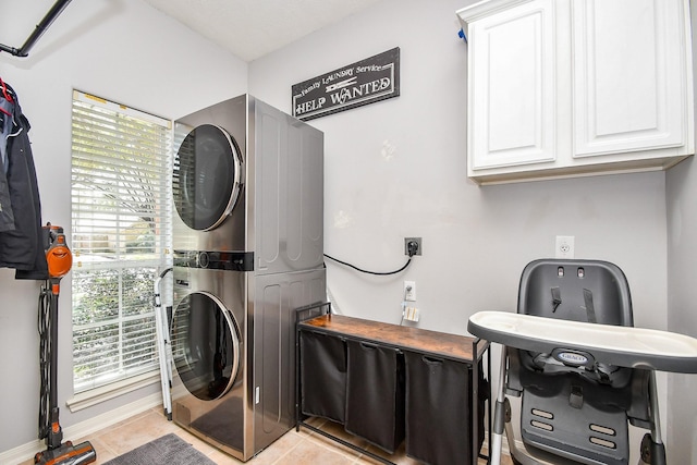 clothes washing area featuring light tile patterned floors, baseboards, cabinet space, and stacked washer / drying machine