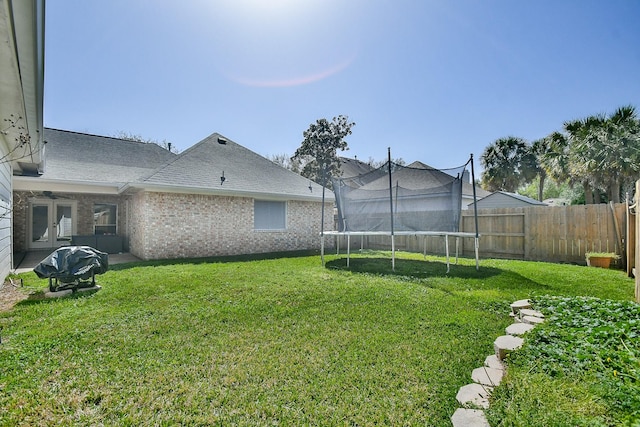 view of yard featuring french doors, a trampoline, and fence