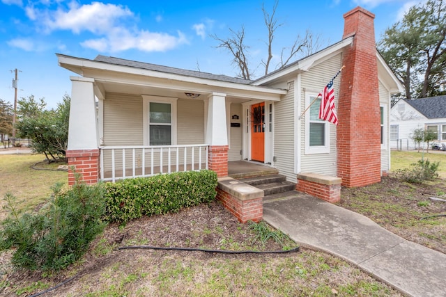 view of front of house featuring a front yard, covered porch, and a chimney