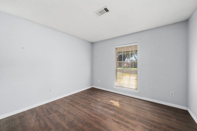 unfurnished room with dark wood-type flooring, visible vents, and baseboards