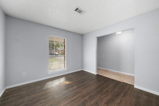 spare room with a textured ceiling, dark wood-type flooring, visible vents, and baseboards