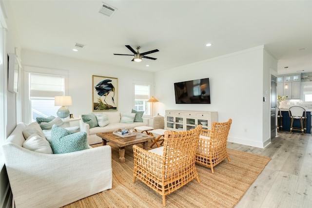 living area featuring light wood finished floors, recessed lighting, visible vents, ornamental molding, and baseboards