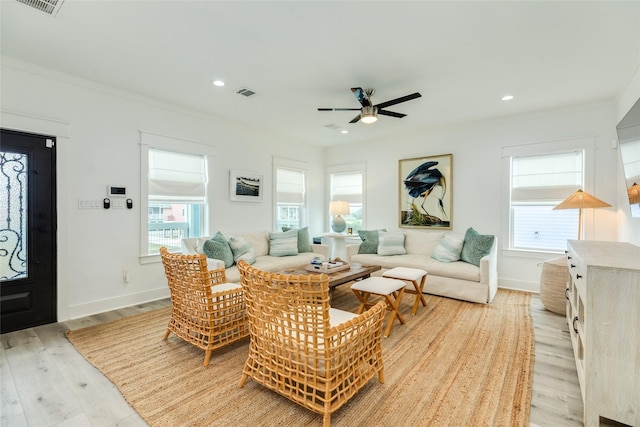 living room featuring light wood-type flooring, visible vents, a wealth of natural light, and ornamental molding