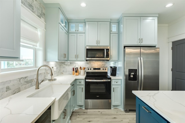 kitchen featuring tasteful backsplash, light wood-style flooring, glass insert cabinets, light stone countertops, and stainless steel appliances