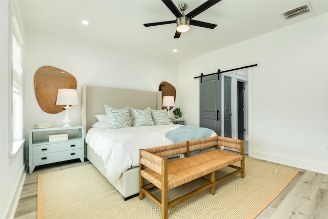 bedroom featuring light wood-type flooring, a barn door, visible vents, and recessed lighting