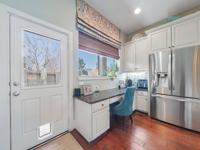 interior space featuring dark stone counters, white cabinetry, dark wood-style floors, built in desk, and stainless steel fridge