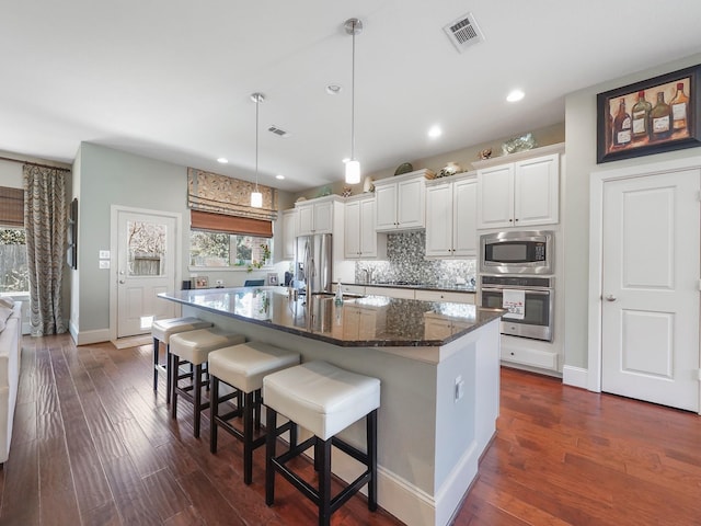 kitchen with stainless steel appliances, a spacious island, visible vents, hanging light fixtures, and dark stone counters