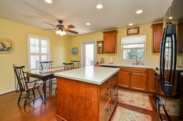 kitchen with a ceiling fan, a sink, light countertops, brown cabinets, and a center island