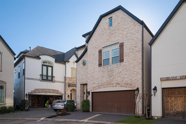 french country style house featuring driveway, brick siding, an attached garage, and stucco siding