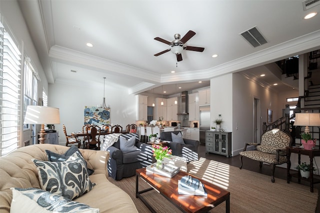 living room with ornamental molding, visible vents, stairway, and ceiling fan with notable chandelier