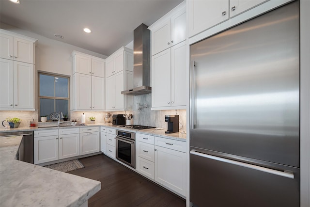 kitchen with white cabinetry, appliances with stainless steel finishes, light stone countertops, wall chimney exhaust hood, and tasteful backsplash