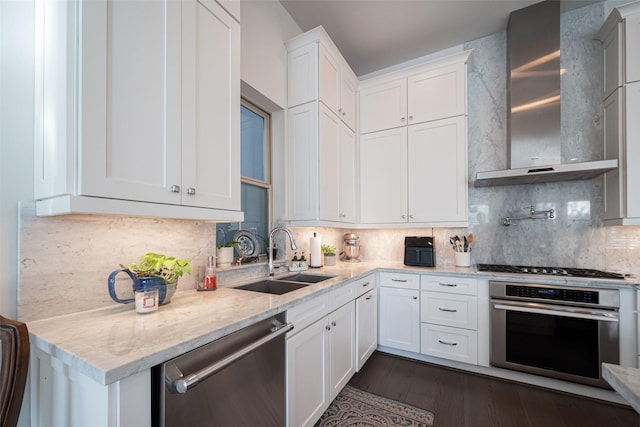 kitchen featuring stainless steel appliances, wall chimney range hood, a sink, and white cabinetry