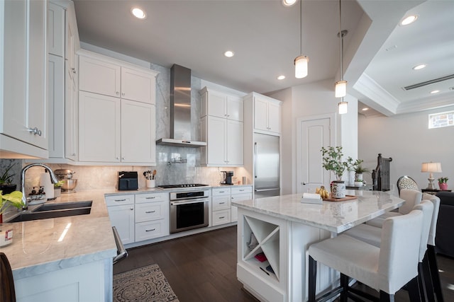 kitchen featuring stainless steel appliances, a kitchen island, a sink, white cabinetry, and wall chimney exhaust hood