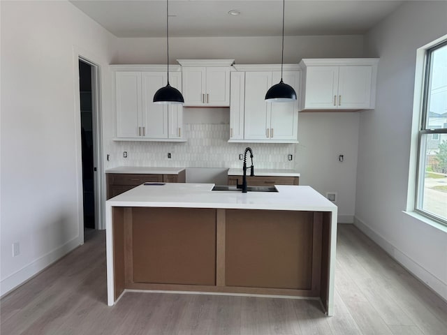 kitchen with backsplash, a center island with sink, white cabinets, and a sink