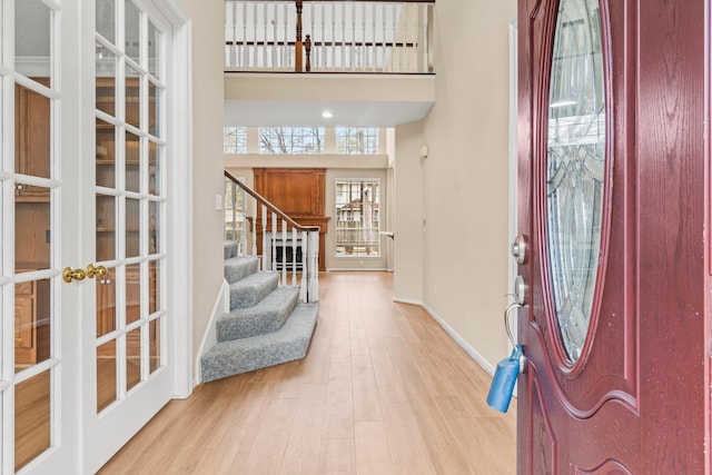 entrance foyer featuring french doors, a towering ceiling, wood finished floors, baseboards, and stairs