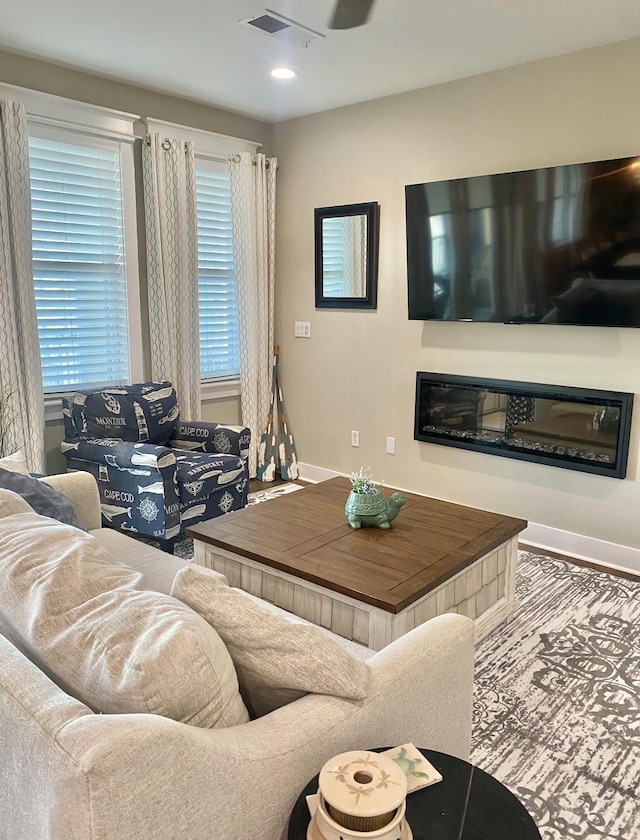 living area with a glass covered fireplace, plenty of natural light, baseboards, and visible vents