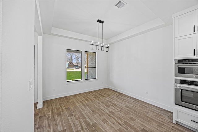 unfurnished dining area featuring visible vents, baseboards, a tray ceiling, light wood-style floors, and a notable chandelier