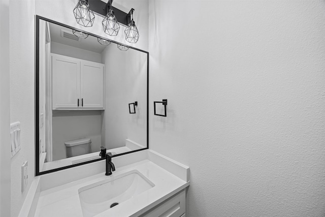 bathroom with toilet, a textured wall, visible vents, and vanity