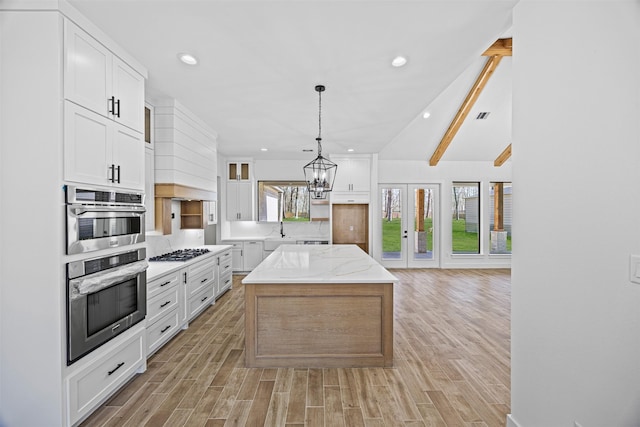 kitchen featuring light stone counters, a center island, pendant lighting, stainless steel gas stovetop, and white cabinets