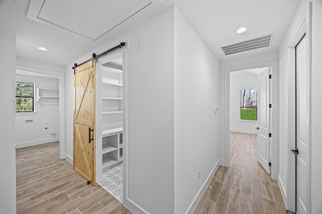 hall featuring a barn door, wood tiled floor, visible vents, and a wealth of natural light