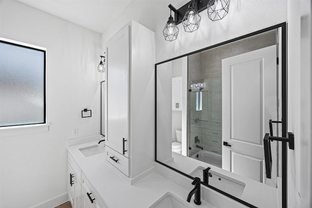 bathroom with toilet, a sink, baseboards, combined bath / shower with glass door, and double vanity